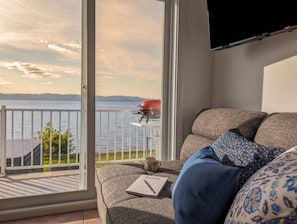 A balcony with a grill, a sofa with a sudoku book, and a TV mounted on the wall.