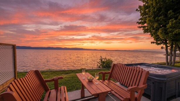 A wooden deck with a hot tub, two wooden chairs, and a table with glasses and a bowl. - Chalet #8 Waterfront | Spa | Fireplace | Wifi | AC (Cap-Saint-Ignace)