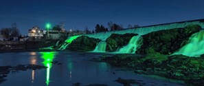 Une cascade illuminée de lumière verte, un mur de pierre et un bâtiment en arrière-plan.
