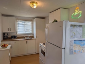 Une cuisine avec des meubles blancs, un four à micro-ondes, un grille-pain, un évier et un réfrigérateur dont la porte est ornée d’une carte.