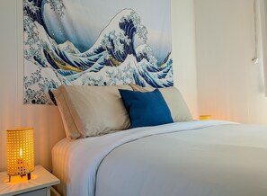 Una habitación de hotel con cama, almohadas, una obra de arte en la pared y una lámpara de noche.