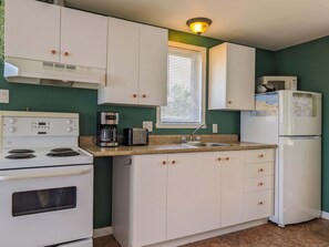A kitchen with white cabinets, a stove, a coffee maker, a toaster, a sink, and a refrigerator. - Chalet #9 Waterfront with Spa, Fireplace, Wifi & AC (Cap-Saint-Ignace)