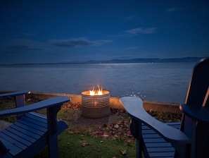 Ein Lagerfeuer mit Blick auf ruhiges Wasser und entfernte Berge.