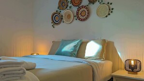 Un letto rifatto con cura, un cuscino, una lampada da comodino e una parete decorata con elementi tessili.
