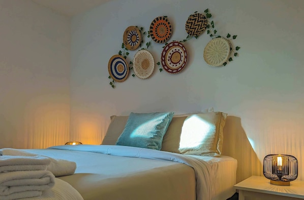 A neatly made bed with a pillow, a bedside lamp, and a wall with decorative woven items.