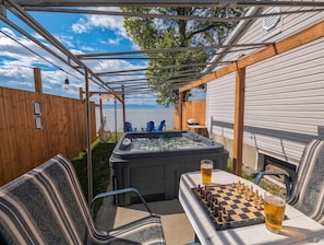 A covered outdoor area with a hot tub, a table with chess and a glass of beer, and chairs.