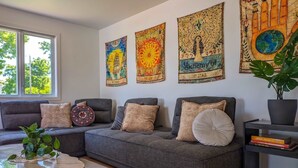 Un soggiorno con un divano grigio, cuscini decorati, un tavolino rotondo e una libreria piena di libri.