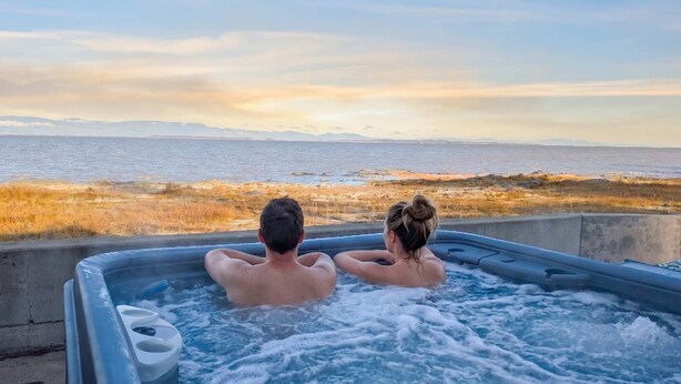 Two people in a hot tub with a view of the sea and distant mountains.