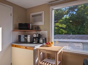A compact kitchen with a microwave, toaster, coffee maker, and a small table with fruit. - Chalet Studio #12 - Relaxing getaway with Wifi & AC (Cap-Saint-Ignace)