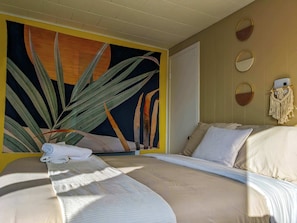 Une chambre avec un lit, un tableau accroché au mur, une porte et un macramé fixé au mur.