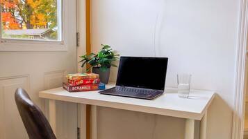 A workspace with a laptop, a neon sign, a potted plant, and board games on a white desk.