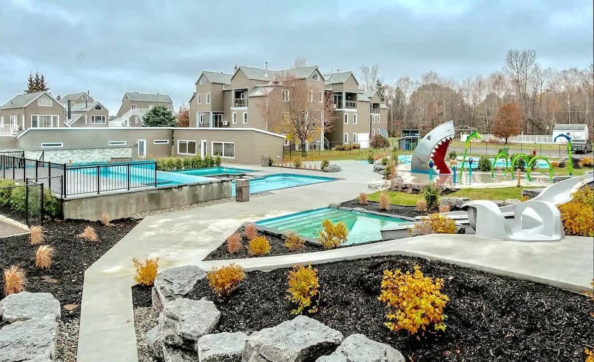 Zona residencial con varios edificios de apartamentos, una piscina y una gran escultura de tiburón.