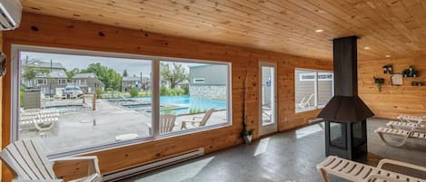 A wooden interior with large windows overlooking a swimming pool and outdoor seating.