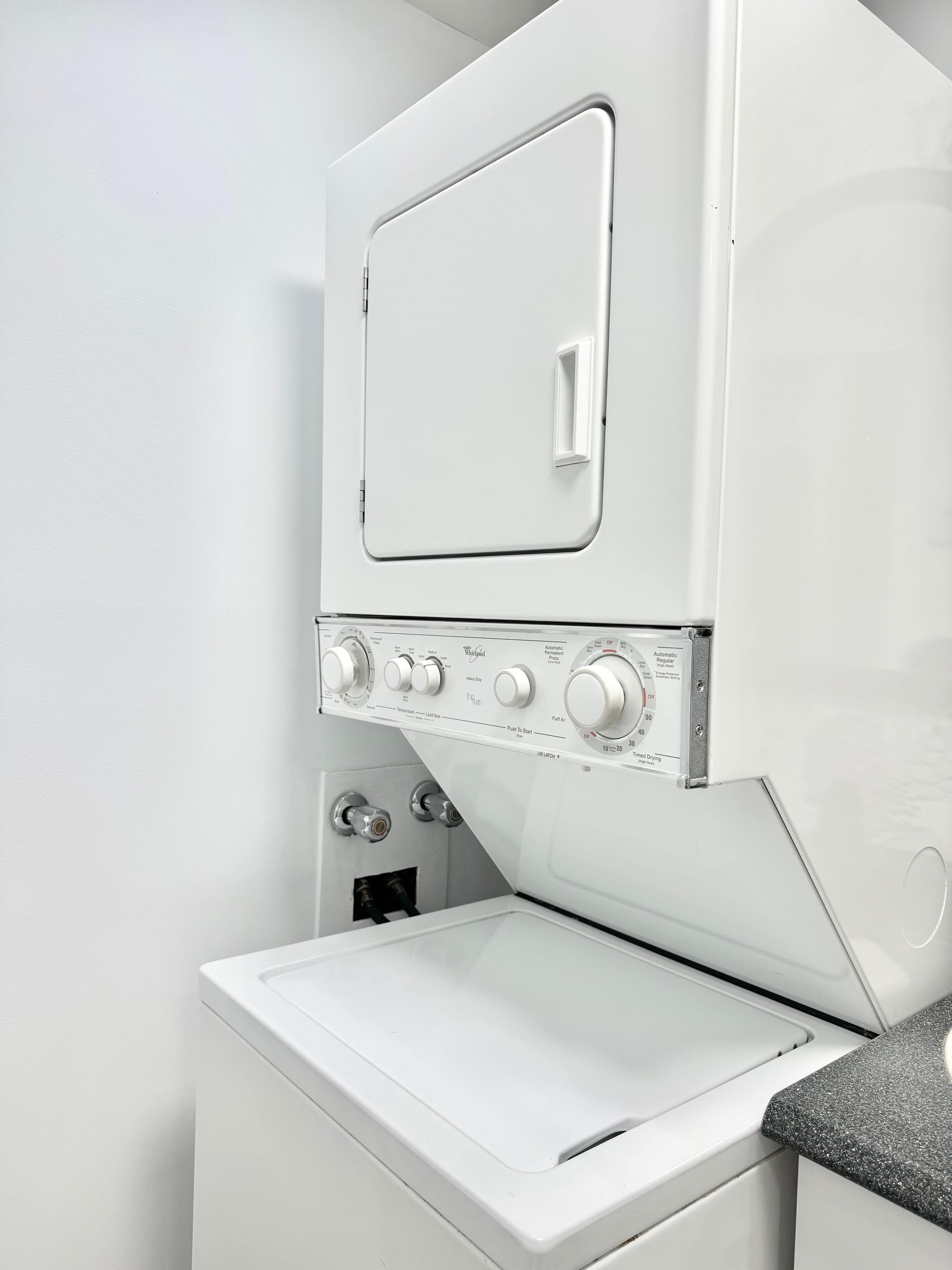 A white washing machine with control knobs and a door, mounted above a white dryer.