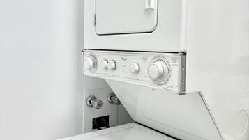 A white washing machine with control knobs and a door, mounted above a white dryer.