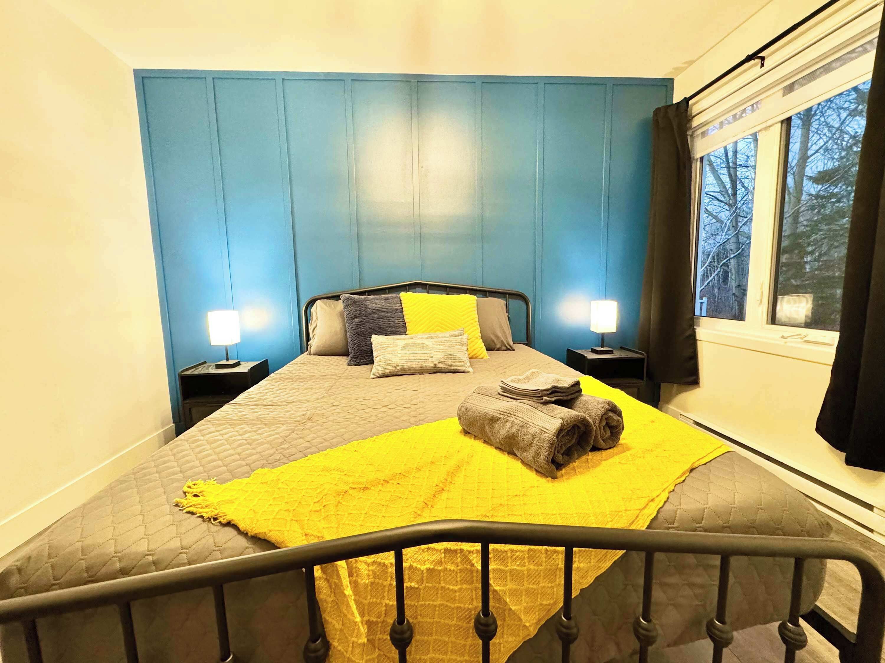 A bedroom with a bed, two bedside tables, a window with curtains, and a view of trees outside.