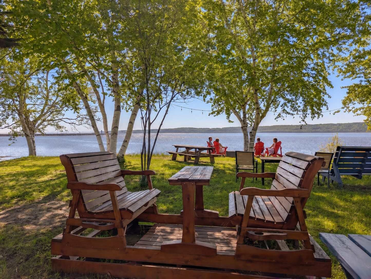 An outdoor seating area with wooden benches and picnic tables, overlooking a lake.