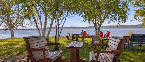 An outdoor seating area with wooden benches and picnic tables, overlooking a lake.