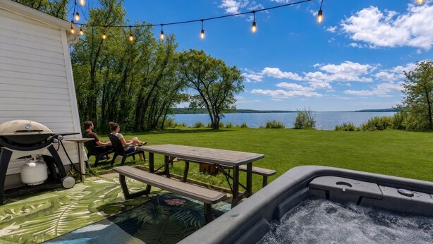 A backyard with a hot tub, picnic table, and string lights. - Riverside Condo w/ Private Hot Tub & Mountain (Sainte-Anne-de-Beaupré)