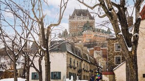 A historic building with a turret and a stone facade, surrounded by leafless trees and snow. - Riverside Condo w/ Private Hot Tub & Mountain (Sainte-Anne-de-Beaupré)