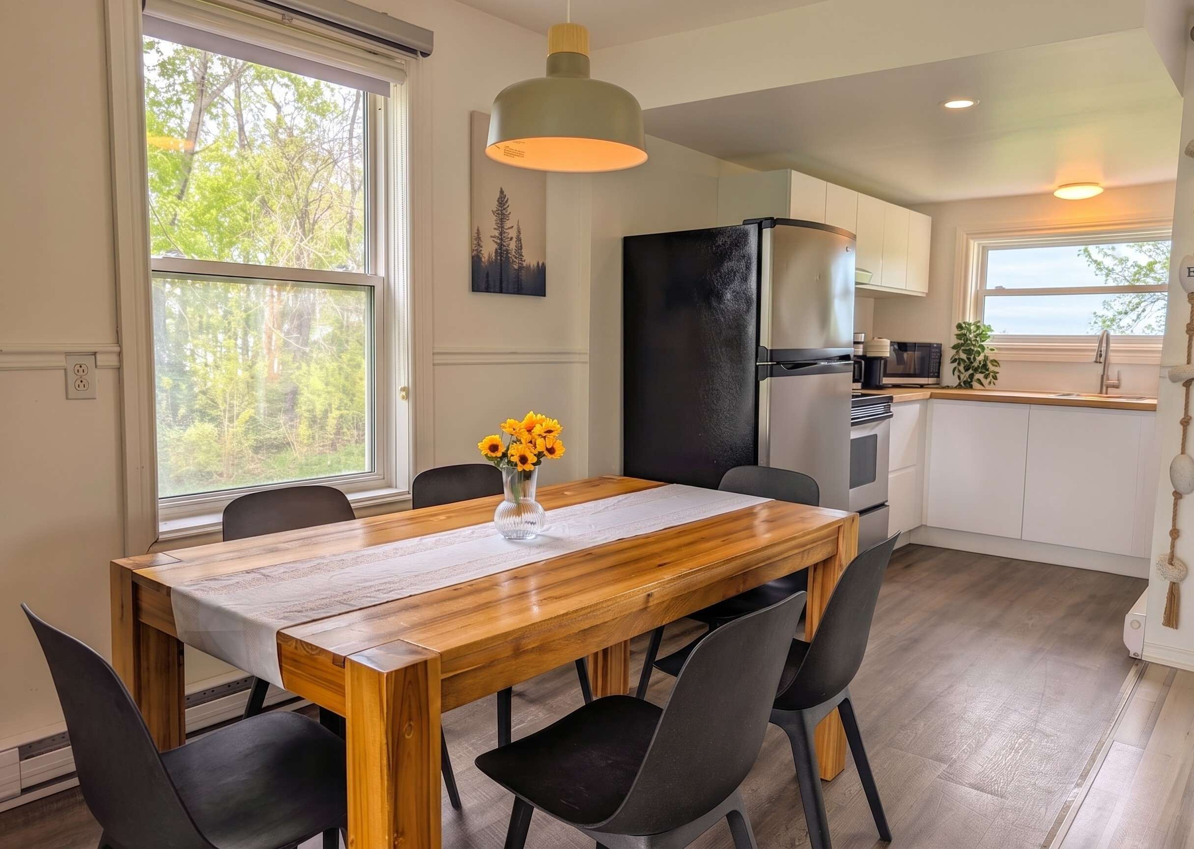 A modern kitchen with a dining area, large windows, and a view of trees.