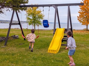 A playground with swings and a slide, located near a body of water. - Condo 1 - Waterfront with SPA, Fireplace & Barbecue (Sainte-Anne-de-Beaupré)