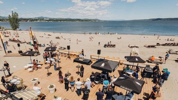 A beachside venue with outdoor seating, umbrellas, and a stage for events.