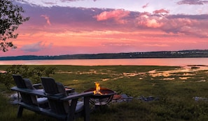 A lakeside view with chairs and a fire pit.