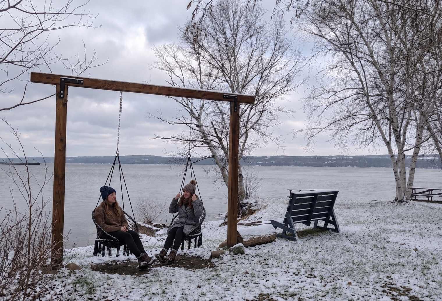Un columpio de madera con dos columpios, un banco y el suelo cubierto de nieve.