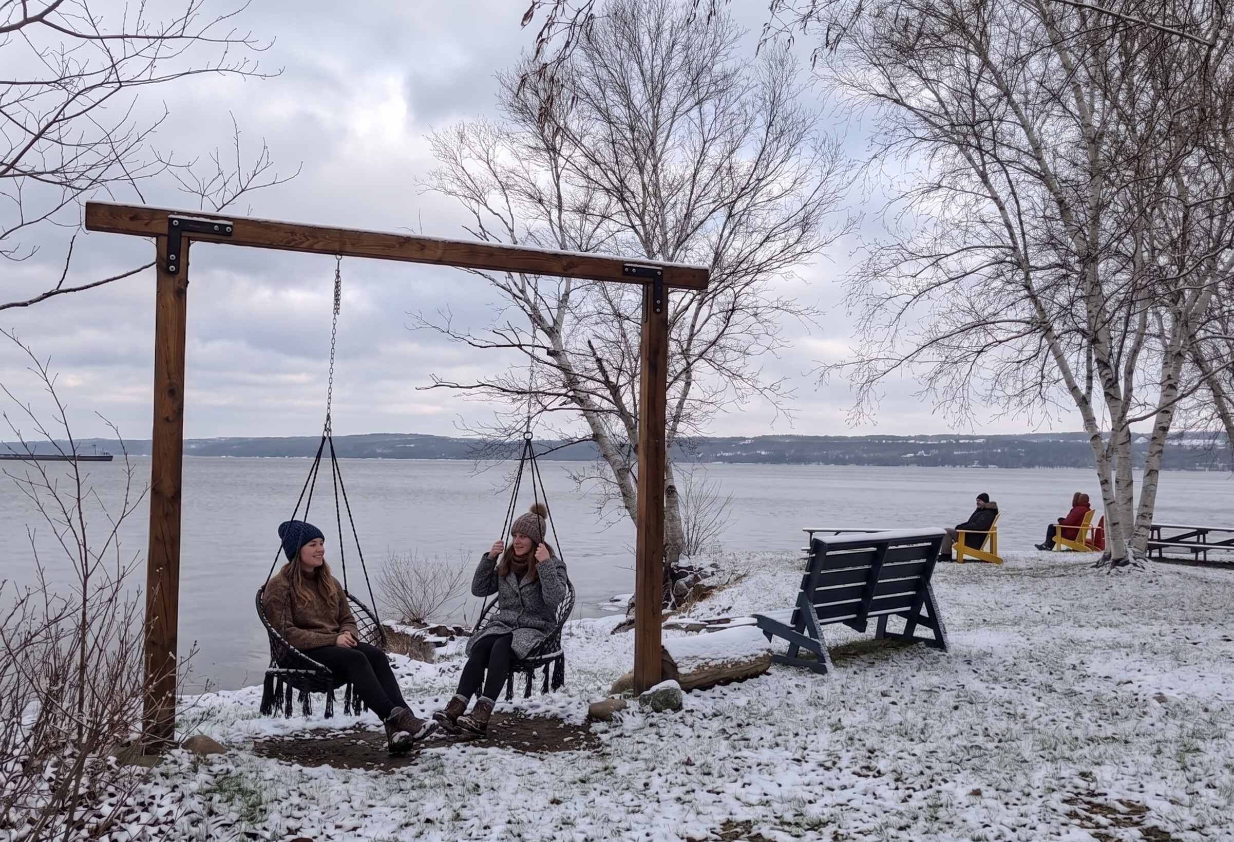 A wooden swing set by a lake with benches and a picnic table nearby.