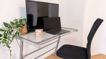A workspace with a laptop on a glass desk, a black chair, and a potted plant.