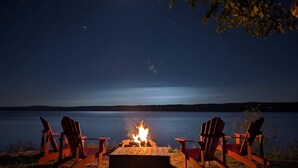 A campfire with chairs around it, overlooking a calm lake at night.