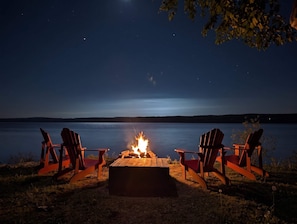 Un feu de camp entouré de chaises, avec une vue sur un lac paisible la nuit.