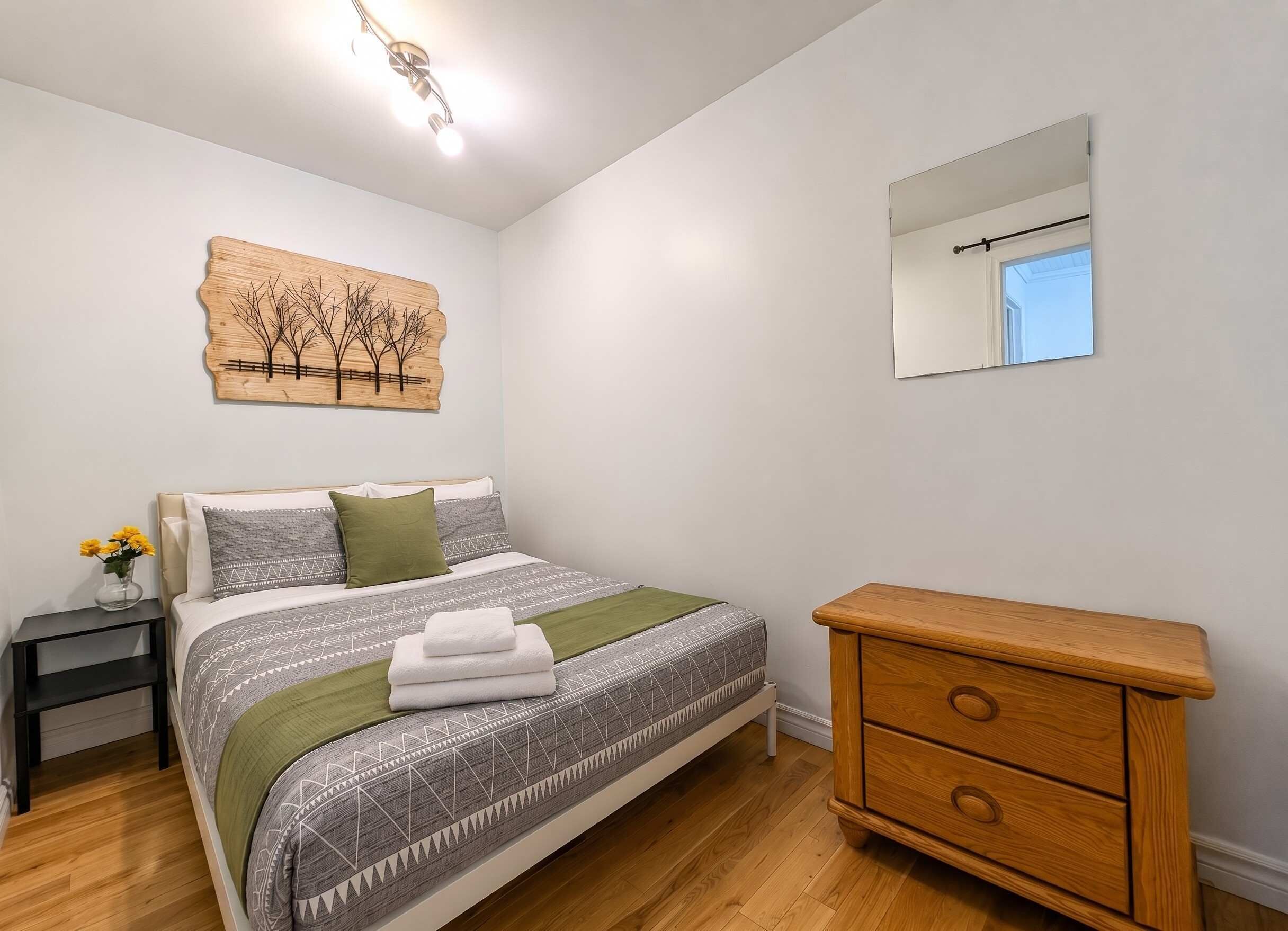 Un dormitorio con cama, mesita de noche, cómoda y espejo en la pared.