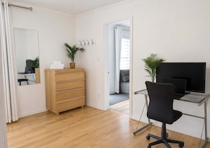 Een kamer met een houten dressoir, een bureau met een computer, een stoel, een spiegel en een potplant.