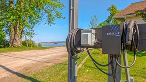 A portable electric vehicle charging station with a cable and a box labeled 'GRIZZLE DUO' by a road with a view of a body of water and trees.