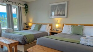 Habitación de hotel con dos camas, bancos de madera, una ventana con cortinas, una lámpara fijada a la pared y un cuadro enmarcado.