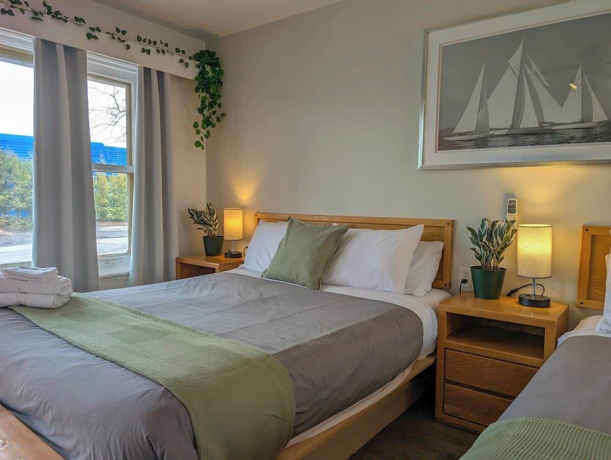 A hotel room with a large bed, two bedside tables with lamps, a window with curtains, and a framed picture on the wall.
