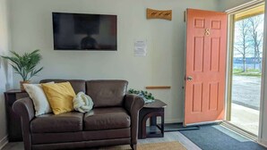 Una sala de estar con un sofá de cuero marrón, un televisor de pantalla plana, un letrero de madera y una puerta con un número.