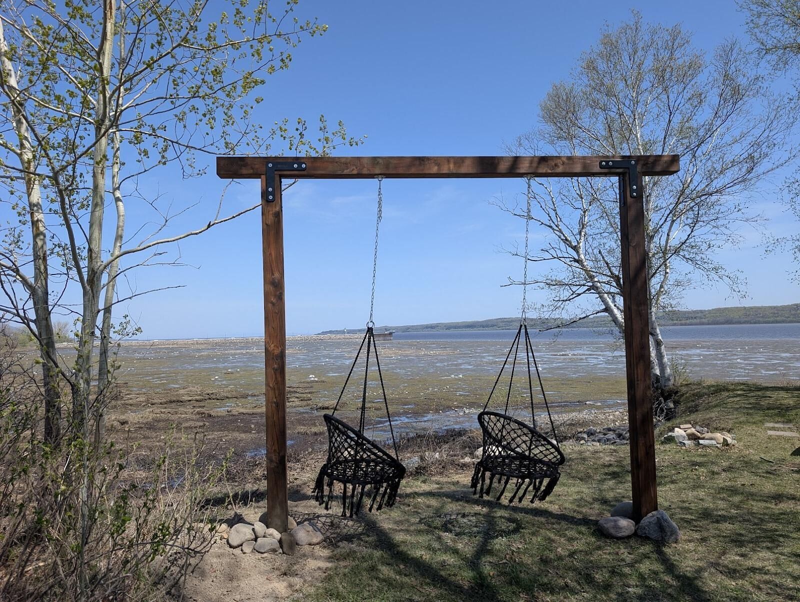 A wooden swing set with two swings in a natural setting.