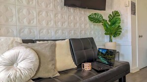 Ein modernes Wohnzimmer mit einer schwarzen Ledersofa, einem wandmontierten Fernseher und einem Blumentopf.