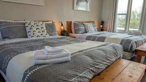 Ein Hotelzimmer mit zwei Betten, jeweils mit gemusterten Bettbezügen und Kissen, einer hölzernen Bank und Blick auf Bäume durch das Fenster.