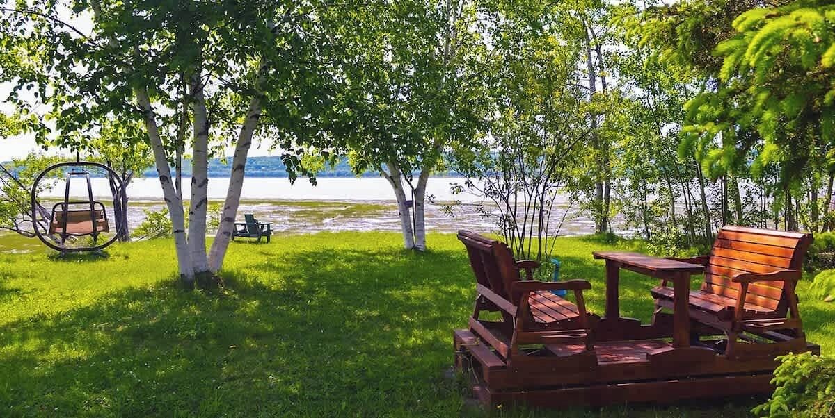 Een houten terras met een schommel, stoelen en een tafel aan een meer.