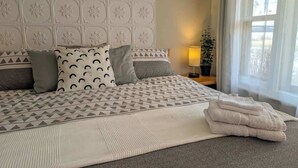 Una cama bien hecha con ropa de cama estampada, una lámpara de noche y una ventana con cortinas.