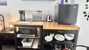 Eine Küche mit Mikrowelle, Toaster, Kaffeemaschine und Kühlschrank. Darüber befinden sich Regale mit verschiedenen Küchenutensilien.