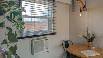 A room with a large window, a table with chairs, a hanging light fixture, and a potted plant.