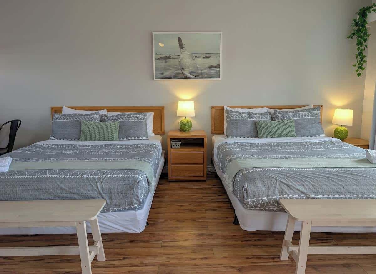Een tweepersoonskamer met twee bedden, elk voorzien van een nachtkastje, een lamp en een klein plankje. Boven de bedden hangt een schilderij aan de muur.