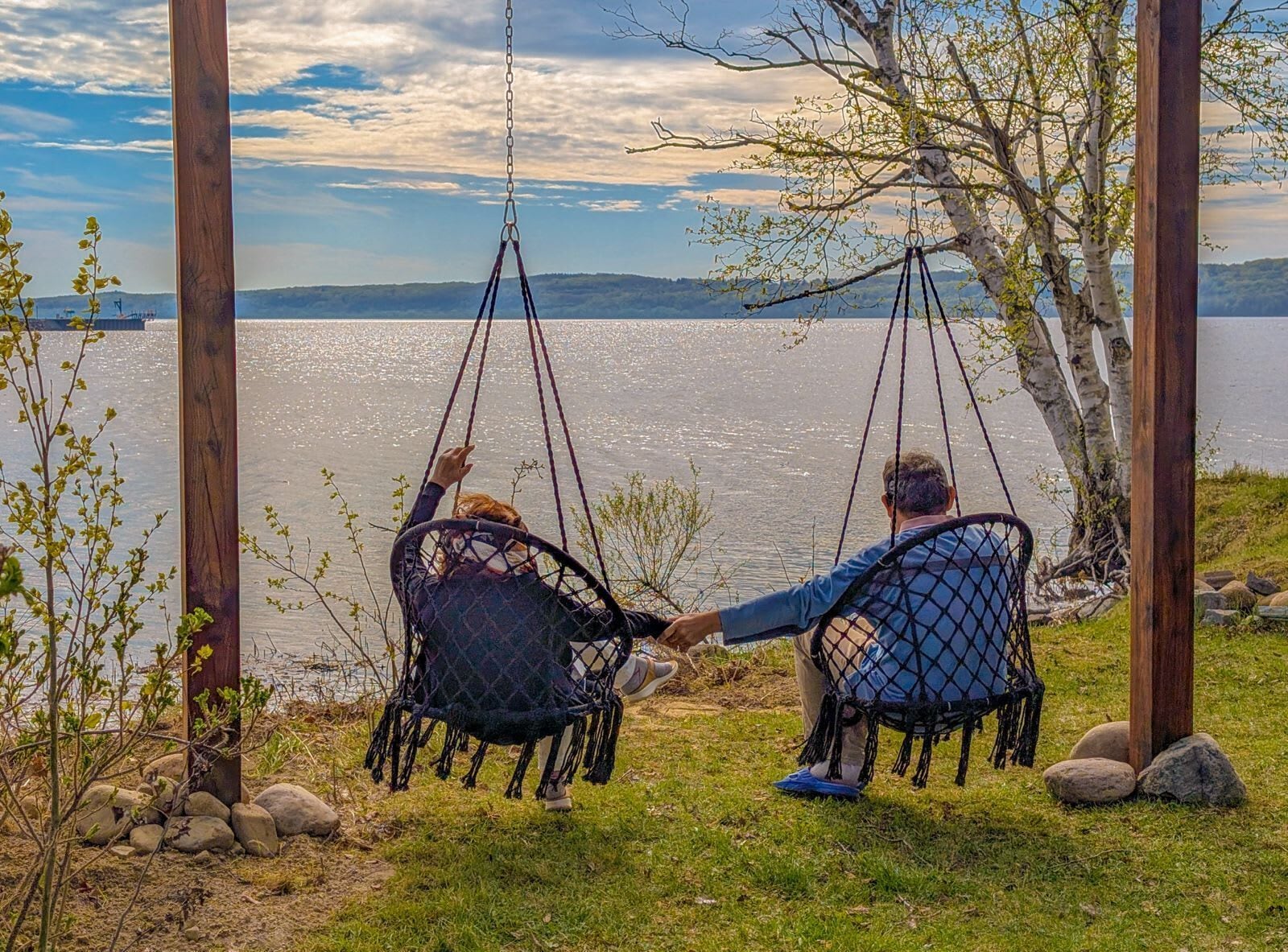 Deux personnes sont assises sur des balançoires, face à un lac, sous un ciel dégagé.