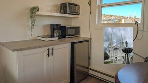 Cocina compacta con microondas, cafetera y refrigerador pequeño. Una ventana muestra vistas de una catedral.