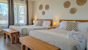 Una habitación de hotel con dos camas, un banco de madera y vistas al exterior.